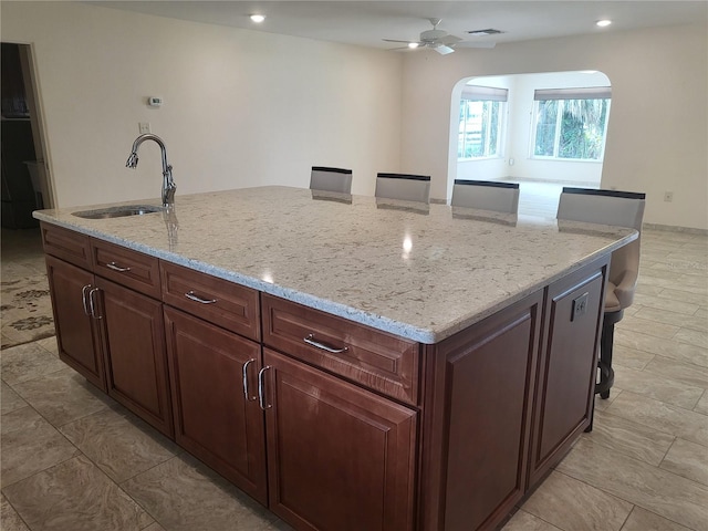 kitchen featuring sink, ceiling fan, light stone countertops, an island with sink, and a kitchen bar