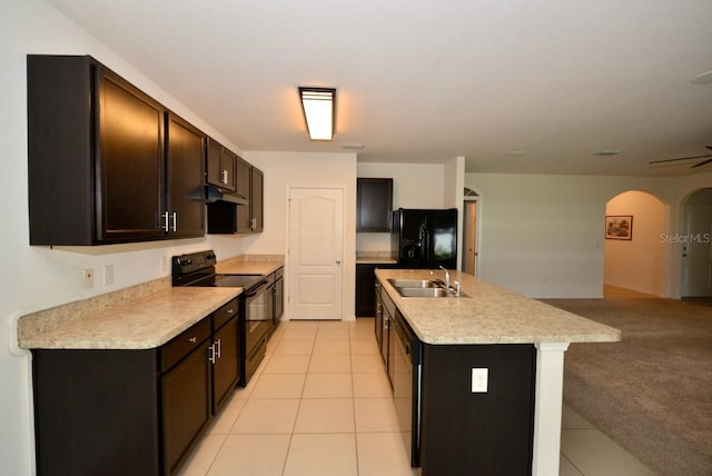 kitchen with light tile patterned flooring, sink, black appliances, dark brown cabinets, and a center island with sink