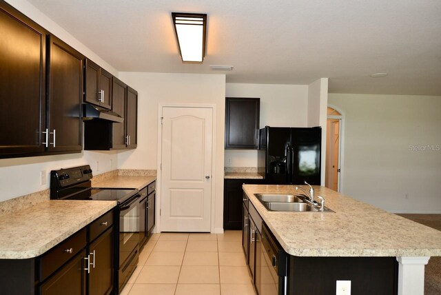 kitchen with sink, dark brown cabinets, light tile patterned floors, an island with sink, and black appliances