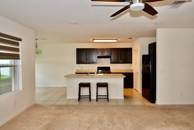 kitchen with an island with sink, sink, stove, light tile patterned floors, and black fridge