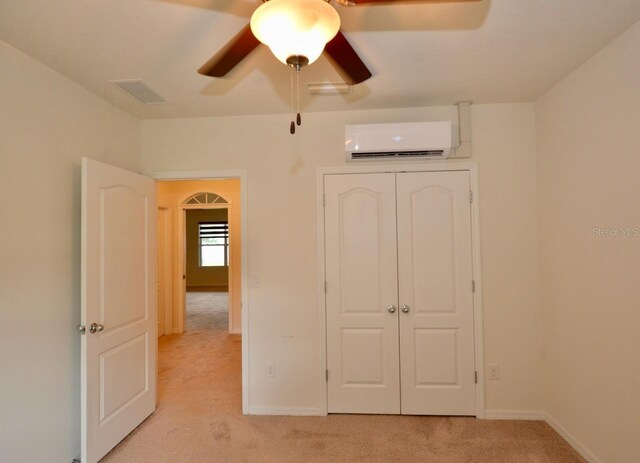 unfurnished bedroom featuring a wall mounted air conditioner, light colored carpet, ceiling fan, and a closet