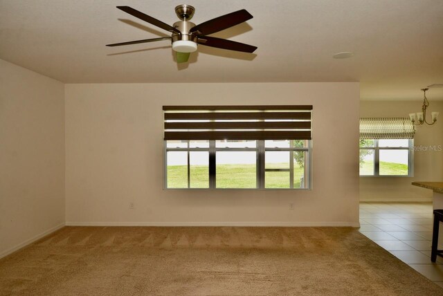 empty room featuring ceiling fan with notable chandelier and light tile patterned floors