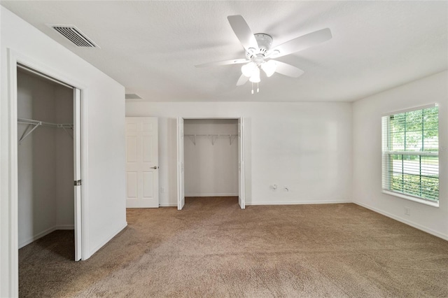 unfurnished bedroom featuring carpet, two closets, and ceiling fan