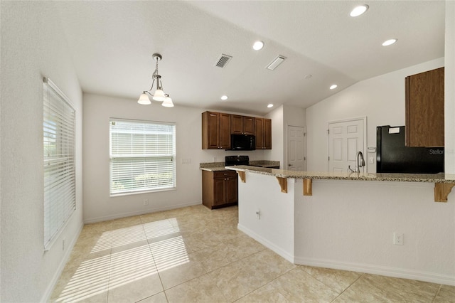 kitchen featuring black appliances, hanging light fixtures, vaulted ceiling, light stone countertops, and a breakfast bar area