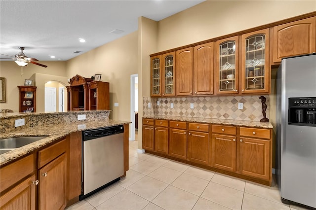 kitchen with tasteful backsplash, light stone counters, stainless steel appliances, ceiling fan, and light tile patterned floors