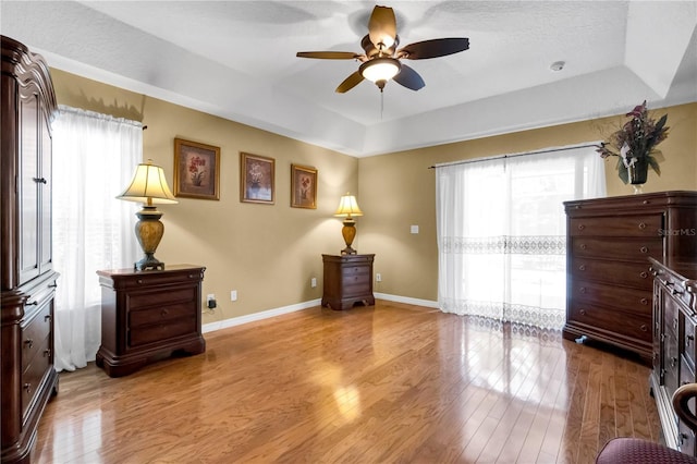 sitting room with light hardwood / wood-style flooring, a raised ceiling, ceiling fan, and a healthy amount of sunlight