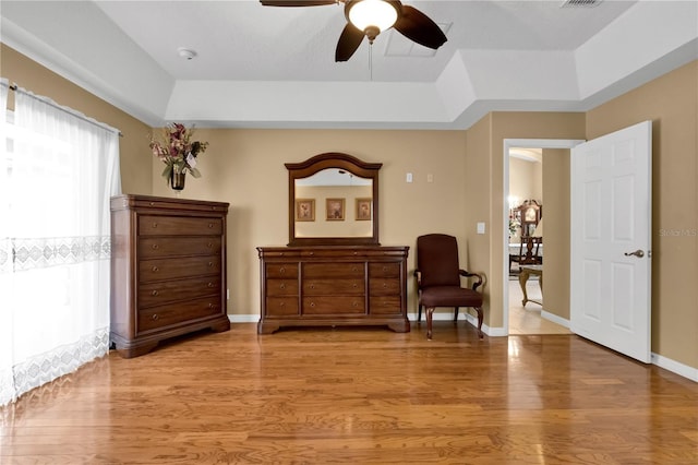 living area with ceiling fan, light hardwood / wood-style floors, and a tray ceiling