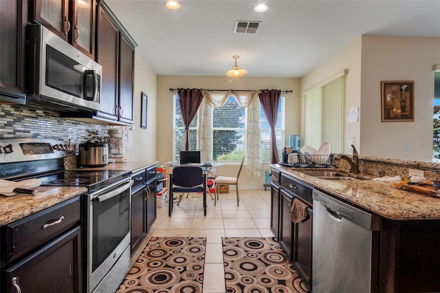 kitchen with appliances with stainless steel finishes, backsplash, sink, light stone counters, and light tile patterned floors