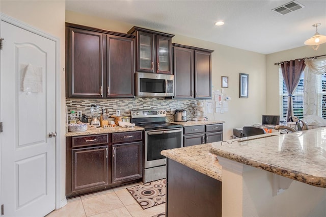 kitchen featuring appliances with stainless steel finishes, tasteful backsplash, light stone counters, pendant lighting, and light tile patterned flooring