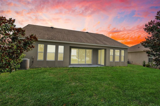 back house at dusk featuring central AC unit and a lawn