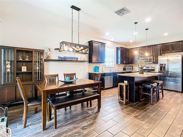 kitchen featuring a kitchen island, a kitchen bar, hanging light fixtures, stainless steel appliances, and dark brown cabinets