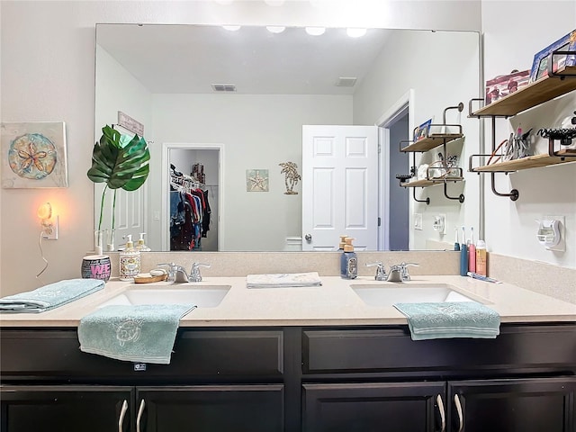 bathroom with double vanity, a spacious closet, visible vents, and a sink