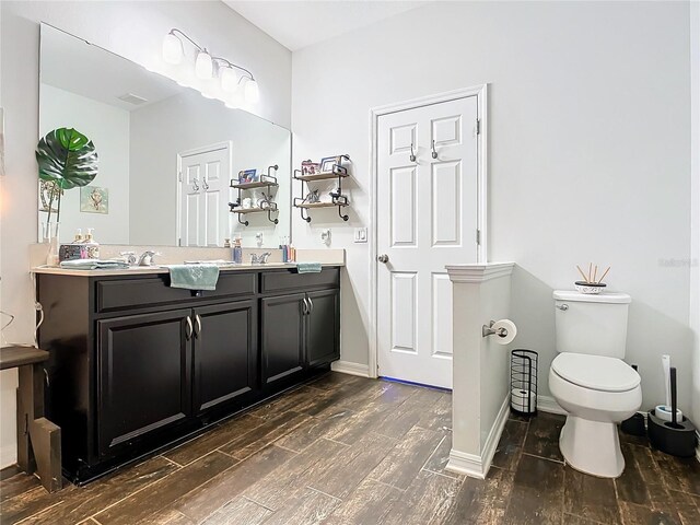 bathroom with double vanity, toilet, a sink, wood finished floors, and baseboards