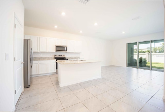 kitchen with light tile patterned floors, light stone counters, a center island with sink, white cabinets, and appliances with stainless steel finishes