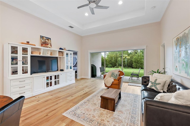 living room featuring a tray ceiling, ceiling fan, light hardwood / wood-style flooring, and a high ceiling