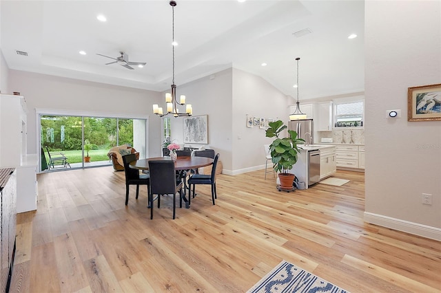 dining room with ceiling fan with notable chandelier, light wood-type flooring, and a raised ceiling