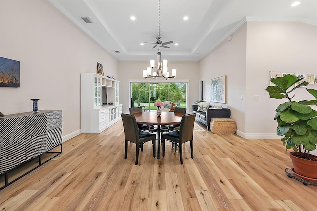 dining room with ceiling fan with notable chandelier, a tray ceiling, light hardwood / wood-style flooring, and ornamental molding