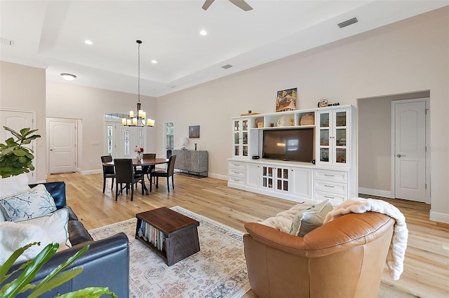 living room featuring a raised ceiling, light hardwood / wood-style flooring, and ceiling fan with notable chandelier