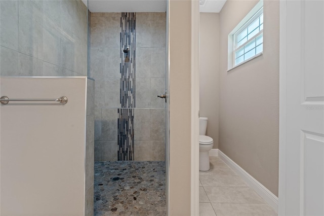 bathroom with toilet, a tile shower, and tile patterned flooring