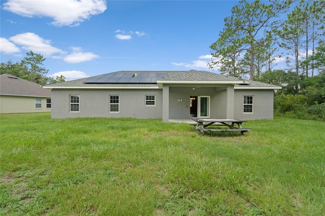 back of house with solar panels and a lawn