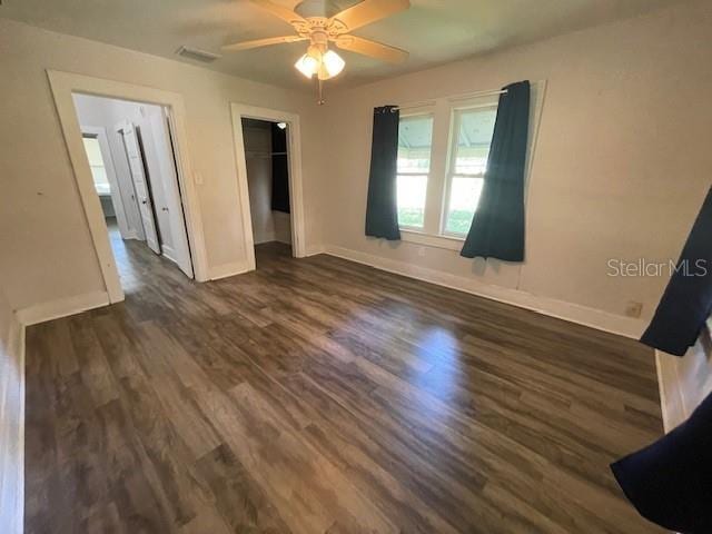 unfurnished bedroom with ceiling fan, a walk in closet, a closet, and dark hardwood / wood-style flooring