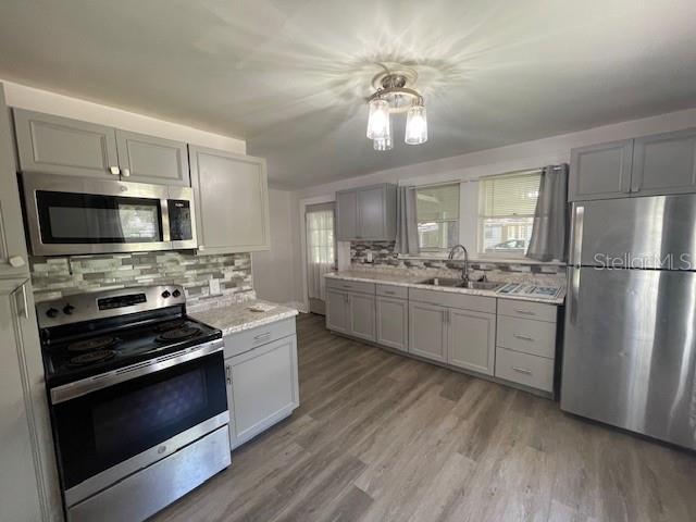 kitchen with tasteful backsplash, gray cabinets, sink, light hardwood / wood-style flooring, and appliances with stainless steel finishes