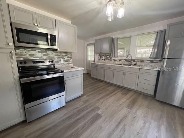 kitchen featuring appliances with stainless steel finishes, gray cabinetry, decorative backsplash, light hardwood / wood-style flooring, and sink