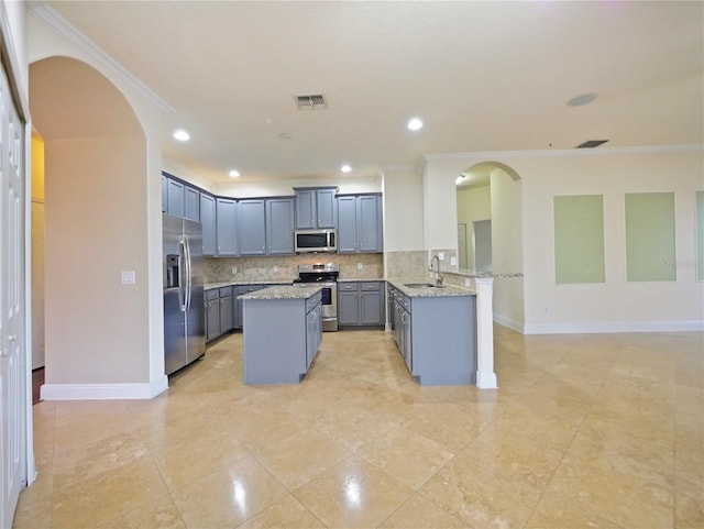 kitchen featuring kitchen peninsula, appliances with stainless steel finishes, tasteful backsplash, light stone counters, and ornamental molding