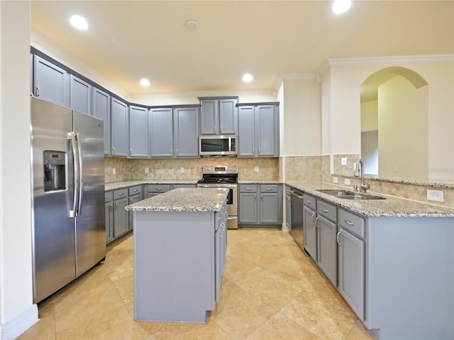 kitchen featuring kitchen peninsula, appliances with stainless steel finishes, light stone counters, ornamental molding, and sink