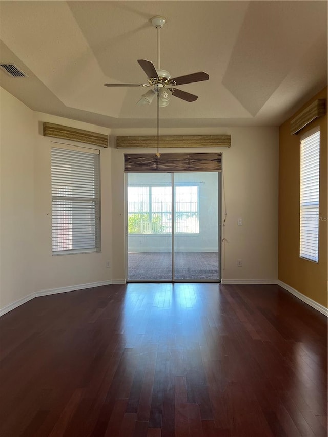 empty room with a raised ceiling, ceiling fan, and dark wood-type flooring