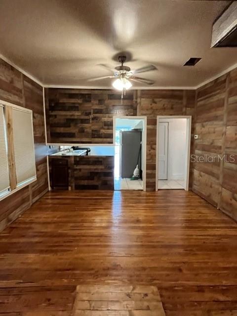 unfurnished living room with hardwood / wood-style flooring, ceiling fan, ornamental molding, and wood walls