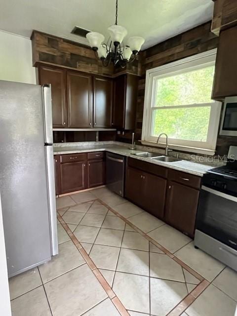 kitchen with stainless steel appliances, sink, light tile patterned floors, decorative light fixtures, and an inviting chandelier