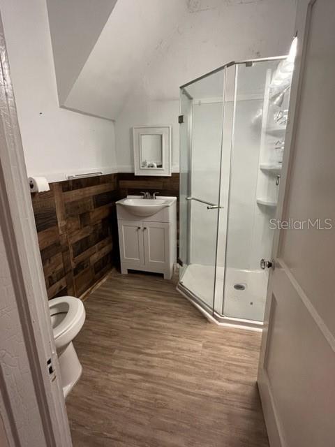 bathroom featuring vanity, a shower with door, wood-type flooring, toilet, and wood walls