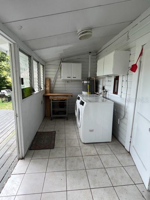 laundry room with wood walls, washer and clothes dryer, light tile patterned flooring, and cabinets