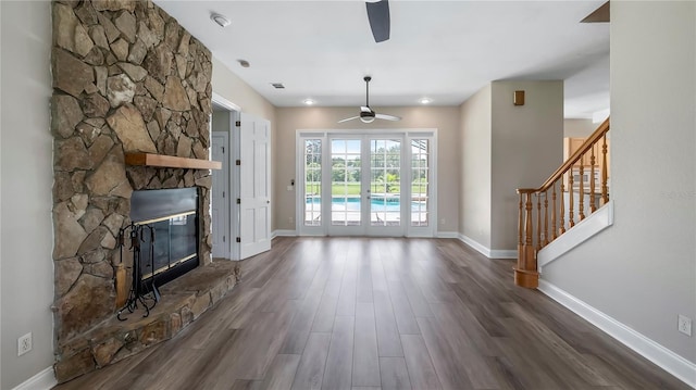 unfurnished living room featuring a stone fireplace, ceiling fan, and dark hardwood / wood-style floors