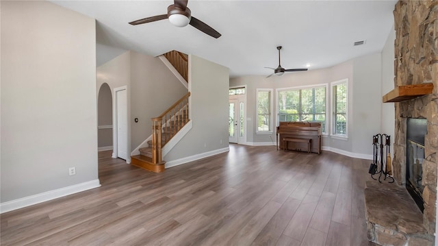 unfurnished living room with hardwood / wood-style floors, a stone fireplace, and ceiling fan