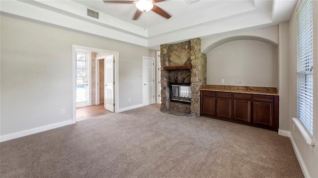 unfurnished living room featuring a fireplace, carpet, a tray ceiling, and ceiling fan