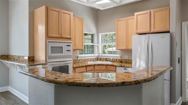 kitchen featuring light stone countertops, sink, coffered ceiling, kitchen peninsula, and white appliances