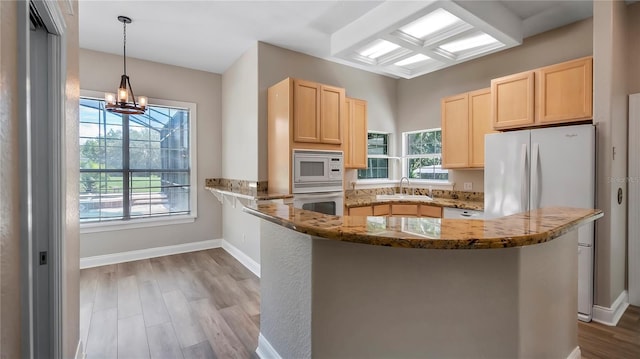 kitchen featuring a notable chandelier, kitchen peninsula, dark stone countertops, pendant lighting, and white appliances