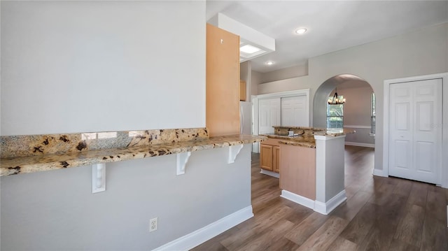 kitchen featuring a kitchen bar, light brown cabinets, kitchen peninsula, and light stone counters