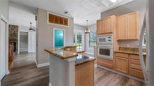 kitchen with wood-type flooring, decorative light fixtures, white appliances, light brown cabinetry, and a center island with sink