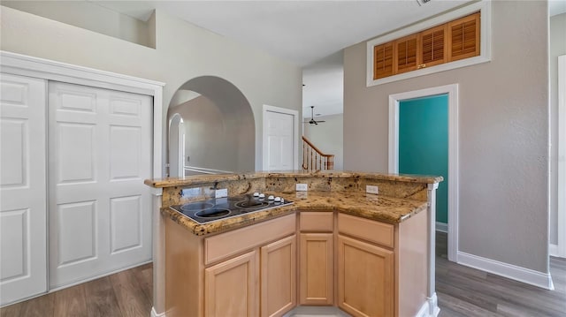 kitchen featuring light brown cabinetry, a towering ceiling, ceiling fan, electric stovetop, and hardwood / wood-style flooring