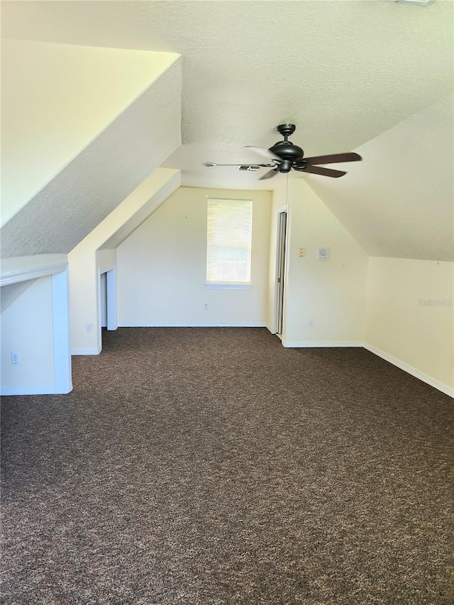 additional living space featuring lofted ceiling, ceiling fan, dark carpet, and a textured ceiling