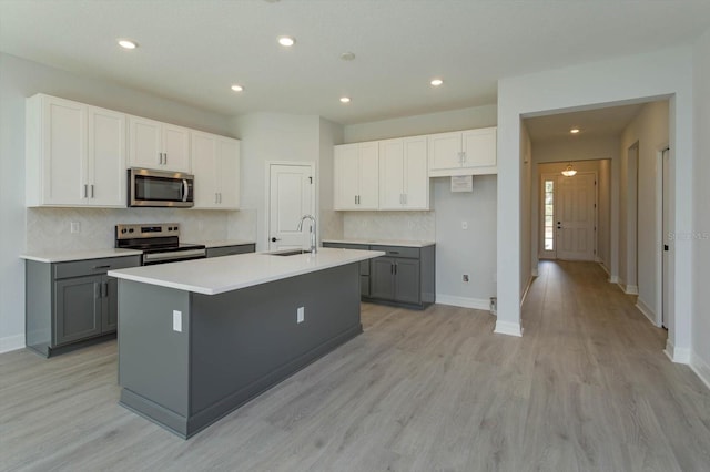 kitchen with gray cabinets, an island with sink, light wood-type flooring, and appliances with stainless steel finishes