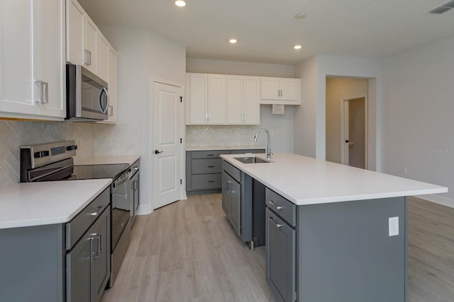 kitchen featuring sink, light wood-type flooring, an island with sink, white cabinetry, and stainless steel appliances