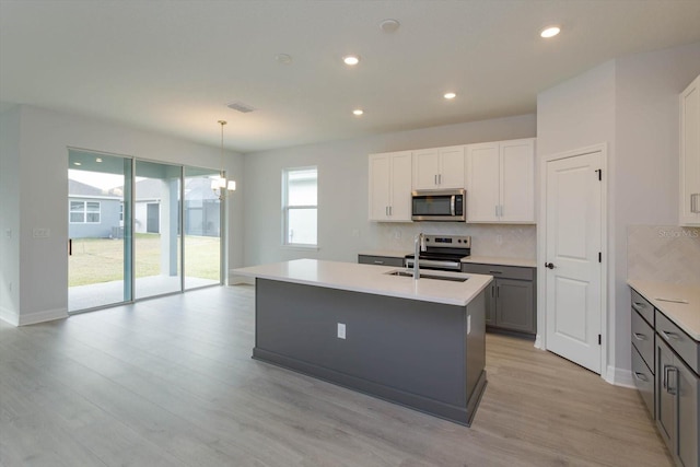 kitchen featuring sink, hanging light fixtures, a center island with sink, appliances with stainless steel finishes, and light wood-type flooring