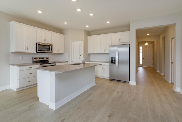 kitchen with a kitchen island with sink, sink, light wood-type flooring, white cabinetry, and stainless steel appliances