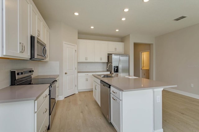 kitchen with appliances with stainless steel finishes, a kitchen island with sink, sink, white cabinets, and light hardwood / wood-style floors