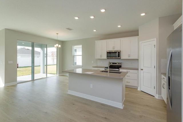 kitchen with stainless steel appliances, pendant lighting, white cabinets, light hardwood / wood-style floors, and an island with sink