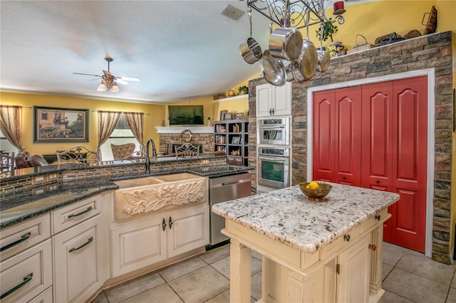 kitchen with stainless steel appliances, a kitchen island, a textured ceiling, cream cabinetry, and light tile patterned floors